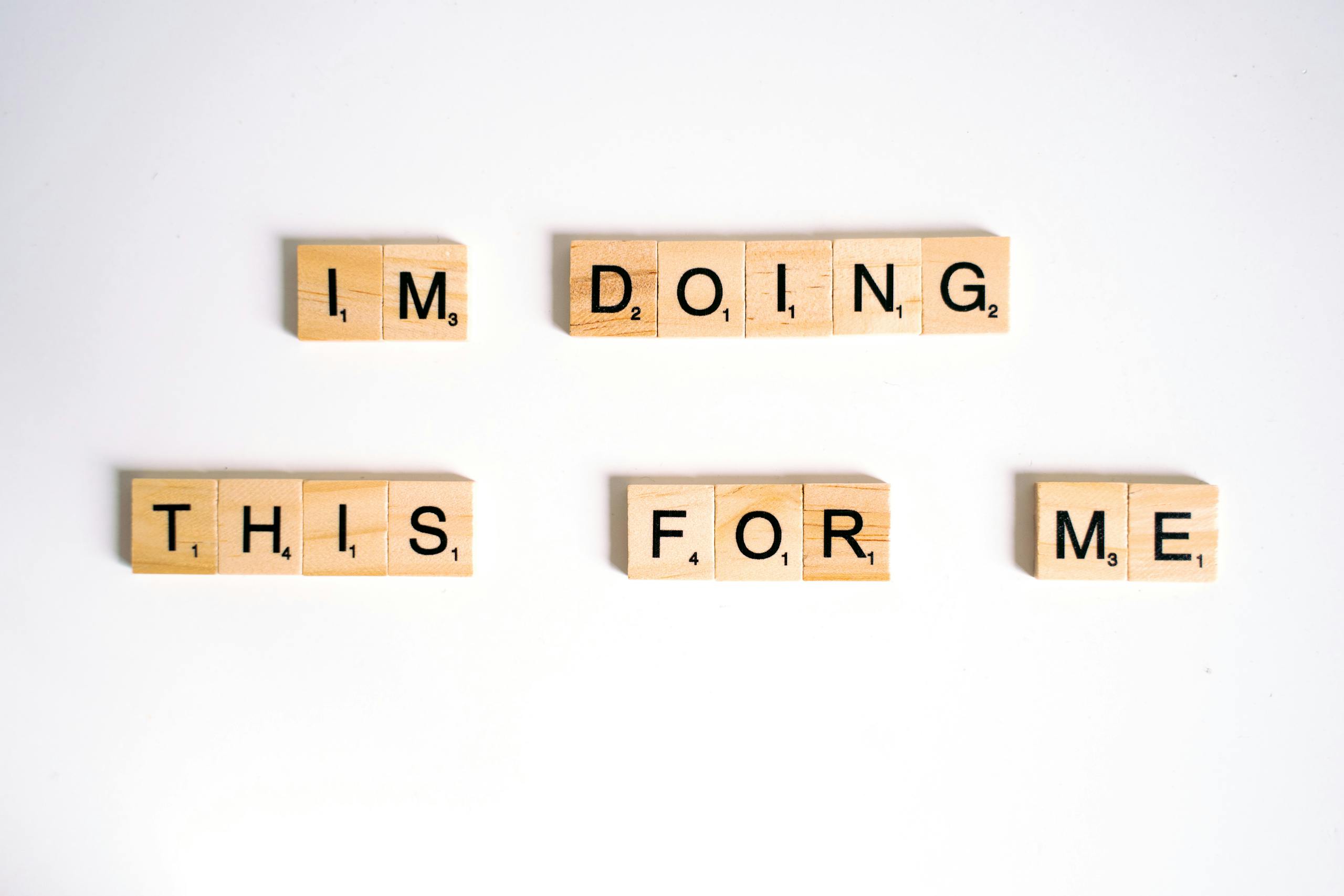 Wooden Scrabble tiles spell 'I'm doing this for me' on a white surface.